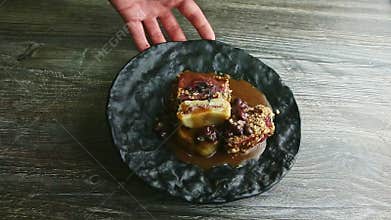 Human hand rotates black plate with meat steak and red bean sauce