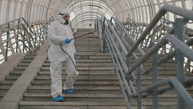 Virologist in protective suit disinfects surface, sprays chemicals on handrails