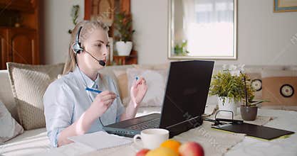 Sales representative in headset speaking to client and making video conference call on laptop.