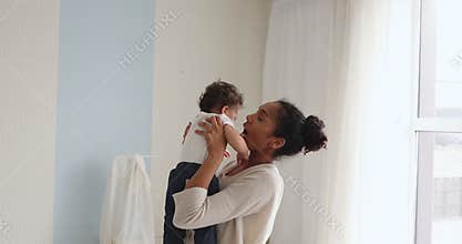 Happy African mom lifting cute infant child standing in bedroom