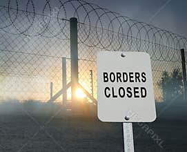 Barbed and razor wire on a fence with a sign `borders closed