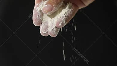 Flour falling from hand in slow motion. Black background.