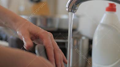 Closeup of a woman`s hands washing dishes in the kitchen under a stream of water