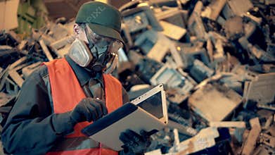 Junkyard employee in a respirator is working with a tablet
