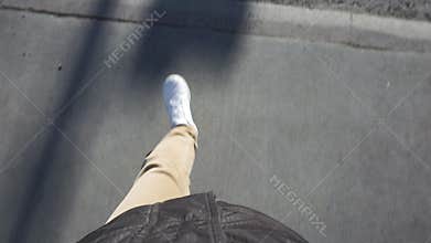 Man walks on the asphalt in white sneakers, crosses the road at a pedestrian crossing