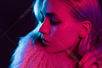 Portrait of millennial pretty fashion girl in fluffy fur coat in pink neon light