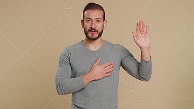 Young man raising hand to take oath, promising to be honest and to tell truth, keeping hand on chest