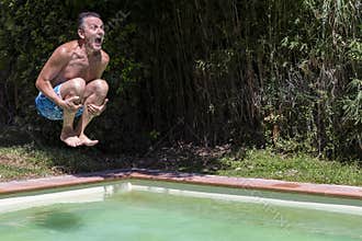 Middle-aged white man dives into swimming pool, cannonball style, with funny expression