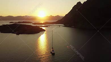 sailboat at sunset, midnight sun, in Lofoten, Norway, with mountains in the distance, yellow and orange sky.