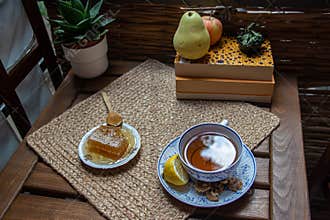 Morning setup on wooden table at balcony for morning relaxation with books, cup of tea, teapot, organic honey, green tea leaves