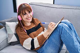 Young woman listening music writing on notebook at home