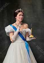 Unhappy birthday. Elegant woman, royal person, queen or princess in white medieval outfit tasting cake on dark vintage
