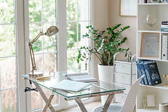 Comfortable workplace with a laptop in the office, at home. Bright room with large windows, bookcase, green plant