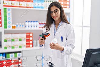 Young hispanic girl pharmacist scanning pills bottle at pharmacy