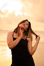 An Asian woman with brown hair and black clothes makes sexy poses very skillfully while enjoying the beach