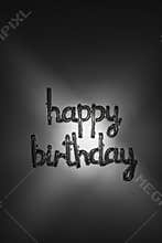 Silver happy birthday balloon lettering with dark, artistic light. Foil letters on vertical background.