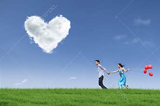 Happy couple running in field with balloons