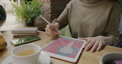 Woman drawing colorful portrait using graphics tablet enjoying digital art at table in cafe