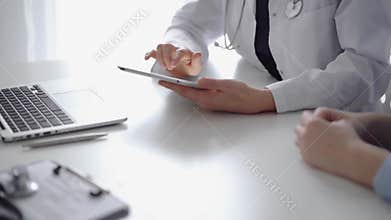 Doctor and patient sitting at the white desk near flair window in clinic. Unknown female physician wearing a white coat