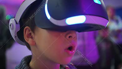 Child in VR glasses opening his mouth in surprise, boy experiencing virtual reality