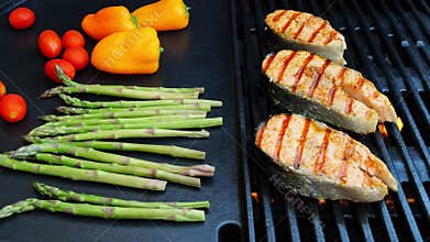 cooking grilled fish steak salmon with asparagus, tomato, pepper on grill, close up, outdoor