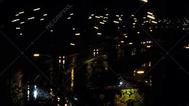 Cars drive along the night road in the rain. Cars headlights and night city lights are reflected on the wet road