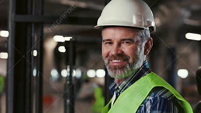 Portrait of Smiling Mature Worker in Safety Vest and Hard Hat. Forklift Driver Looking at Camera. Warehouse with Shelves
