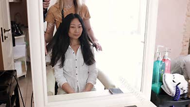 The hairdresser cuts the bangs of a asian girl with scissors in a hairdressing salon.