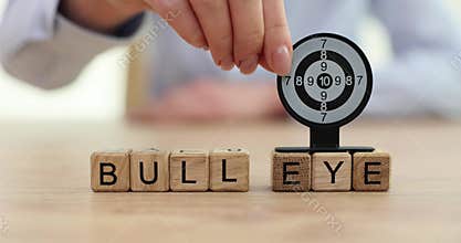 Woman hand places toy model of dart board on word Bull Eye