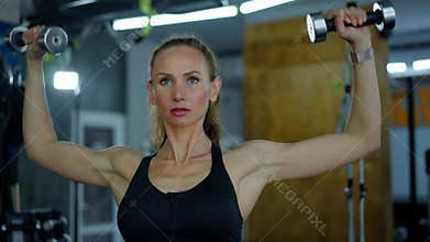 A young girl athlete in the gym does exercises with dumbbells, lifts, bends and straightens her arms. Showing confidence
