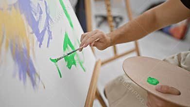 Handsome young hispanic man, an aspiring artist, passionately drawing in the heart of his art studio, carefully holding his