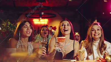 Happy New Year. Beautiful young women in stylish dresses celebrating in bar, counting time to new year. Christmas