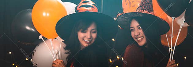 Banner cover design of two beautiful young woman in witch Halloween costumes holding balloons in party over dark magic background