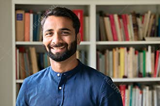 Happy indian business man teacher standing in front of bookshelves, portrait.