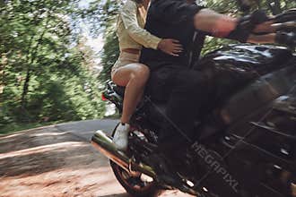 Blurred Motion A young happy couple rides a motorcycle on an asphalt road in the forest, freedom and speed, in motion