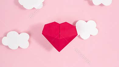 Volumetric origami heart swaying flies between white clouds. Greeting card. Pink background.
