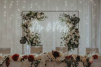 Table topped with flowers and greenery next to a neon sign with Mr and Mrs writings