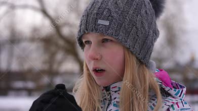 Teenage freezed girl rubbing hands breathing standing outdoors on cold winter day. Close-up portrait of Caucasian