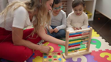 Teacher with boy and girl learning maths with abacus sitting on floor at kindergarten