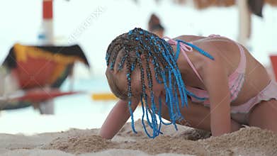 Pretty child girl in bikini swimsuit playing with sand in umbrella shadow during summer tropical vacation