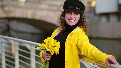 Young smiling woman in a yellow raincoat with daffodils outdoors