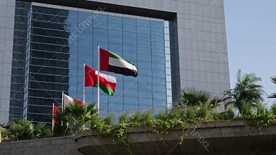 National flags of UAE, Oman, and Bahrain waving in front of a modern glass building in Dubai, UAE. A symbol of Gulf