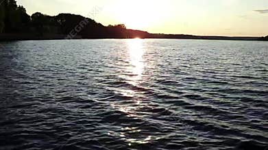 Calm sunset on the lake with play of waves and golden reflection.