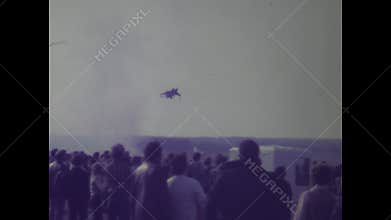 Spectators watch a military jet performing aerobatics at an air show