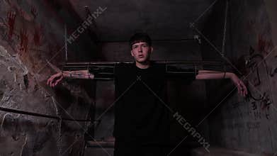 A young man is chained to horizontal handcuffs in a dark quest room.