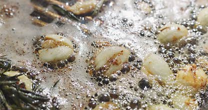 barbecue party, garlic and thyme languish in butter in a frying pan for meat steaks, oil bubbles are illuminated by