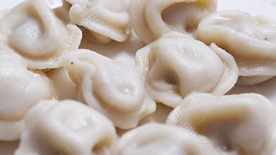 Boiled dumplings with dill are arranged in a circle on a white plate.