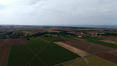 Aerial view of vast farmlands and coastline with expansive horizon under cloudy sky