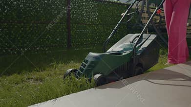 Woman skillfully mows grass along curbs and edges with electric lawn mower