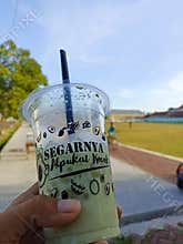Yogyakarta-infonesia, august 24 2025 : Drink in a plastic cup with a straw in hand. Outdoor background